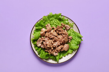 Plate with delicious canned tuna and fresh lettuce on lilac background