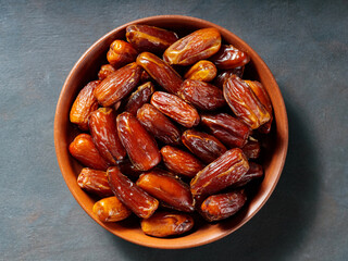 Pitted dates on a clay plate. Bowl with delicious dried dates on a dark background. Ramadan kareem. Top view. Copy space