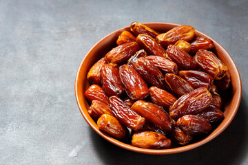 Pitted dates on a clay plate. Bowl with delicious dried dates on a dark background. Ramadan kareem. Top view. Copy space