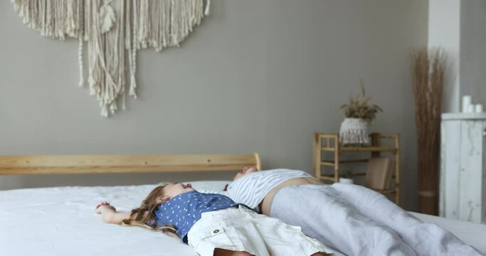Happy playful young mom and little daughter kid sitting on bed, falling down on soft mattress, smiling, laughing, enjoying family leisure time, relaxation in bedroom, having fun Generative AI