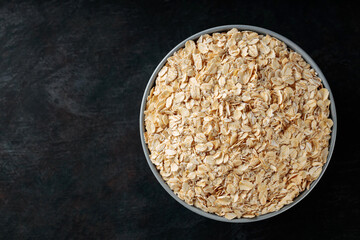 Oat flakes bowl on a dark background. Dry rolled oatmeal for a healthy breakfast. Top view. Copy space