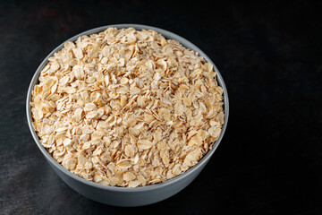 Oat flakes bowl on a dark background. Dry rolled oatmeal for a healthy breakfast. Top view. Copy space