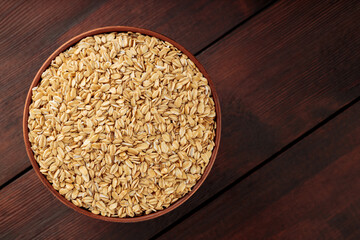 Dry oat flakes in a clay bowl on a wooden background. Dry rolled oatmeal on wooden boards. Healthy eating concept. Copy space. Top view