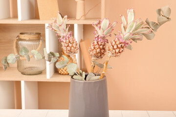 Vase with decorative pineapples and eucalyptus branches on table in room, closeup