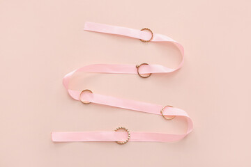 Pink ribbon with golden rings on beige background