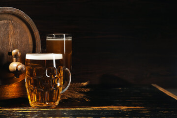 Mug of cold beer and wooden barrel on dark background