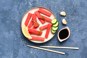 Plate with tasty crab sticks and sauce on blue background