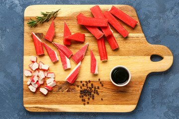 Wooden board with tasty crab sticks and sauce on blue background © Pixel-Shot