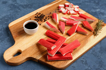 Wooden board with tasty crab sticks and sauce on blue background © Pixel-Shot