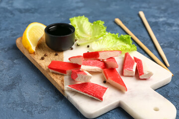 Board with tasty crab sticks on blue background © Pixel-Shot