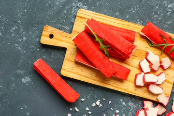 Wooden board with tasty crab sticks on green background © Pixel-Shot