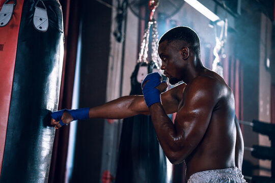 Boxing training of athlete african american man punching a bag at muay thai gym. Active male workout sport club for cardio and body strength. Health and lifestyles concept.