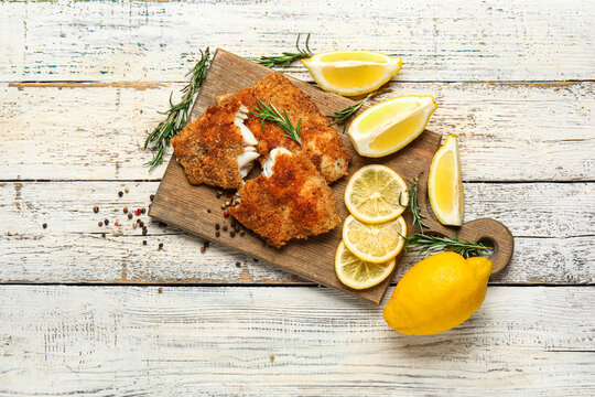 Board of tasty fried codfish with lemon on light wooden background