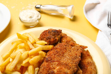 Plate of tasty fried codfish with french fries on yellow background, closeup
