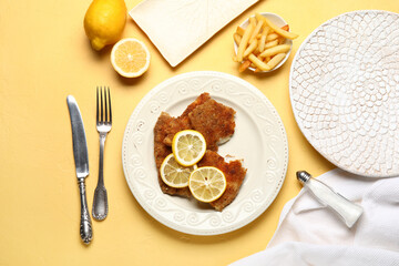 Plate of tasty fried codfish with lemon and french fries on yellow background