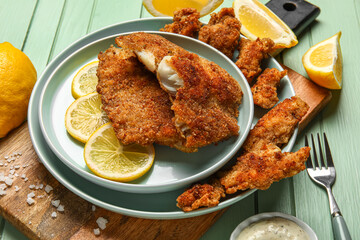 Plates of tasty fried codfish with lemon on green wooden background