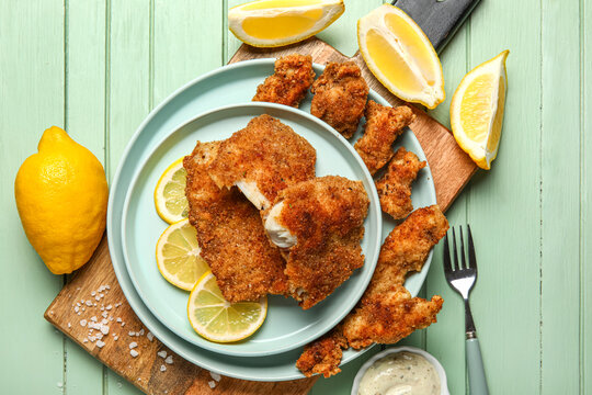 Plates of tasty fried codfish with lemon on green wooden background
