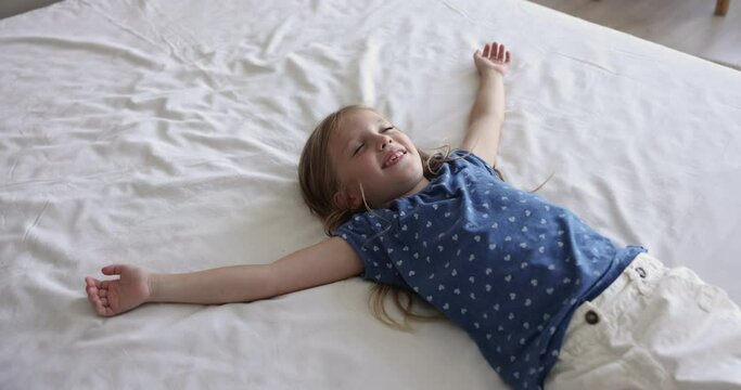 Cheerful cute girl kid sitting on double bed in bedroom, falling on back on soft mattress, enjoying laziness, relaxation, playing active game, lying on white linen, blanket, smiling with Generative AI