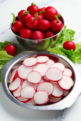 Bowls with fresh slices of radish and lettuce on marble background
