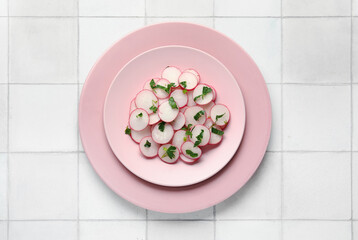 Plates with fresh slices of radish on light tile background