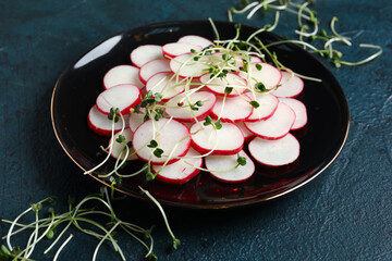 Plate with fresh sliced radish and microgreens on blue grunge background