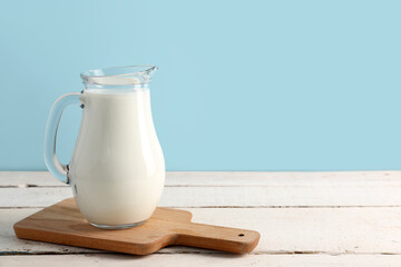 Jug with fresh milk on white wooden table