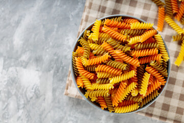 Dry pasta in bowl on a gray background. Three colors fusilli pasta on a linen napkin. Copy space