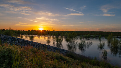 Sunset behind levee with high water next to levee flooding trees