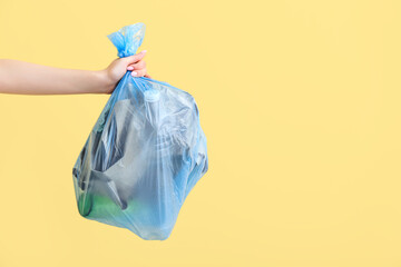 Female hand holding full garbage bag on yellow background - obrazy, fototapety, plakaty