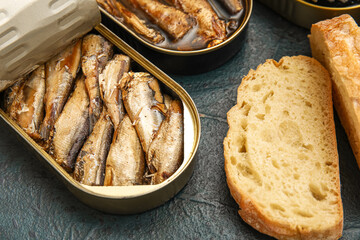 Opened tin cans with sprats in oil and bread on black table