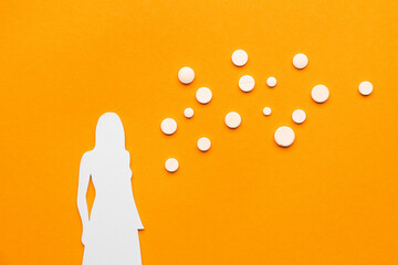 Paper female figure with hormonal pills on orange background