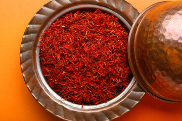 Bowl with pile of saffron on orange background