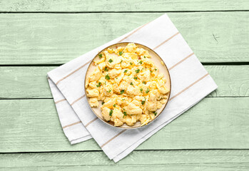 Plate of scrambled eggs with napkin on green wooden background