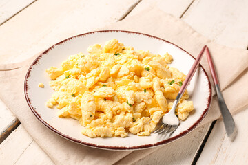 Plate of tasty scrambled eggs with cutlery on white wooden background