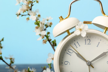Blooming spring branches and white alarm clock on blue background
