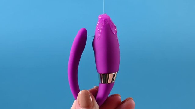 A woman holds a curved sex toy in lubrication on a blue background. Vaginally clitoral vibrator.