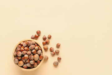 Bowl with shelled hazelnuts on beige background