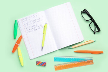Copybook with maths formulas, glasses and stationery on green background