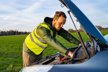 Young man in yellow reflective vest examining his car engine parked on the side of a road
