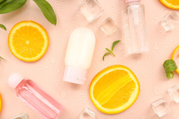 Cosmetic bottles with orange slices, ice cubes and mint on beige background