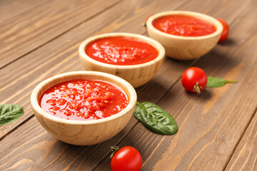 Bowls with tasty tomato sauce and fresh vegetables on wooden background