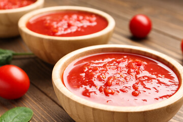 Bowl with tasty tomato sauce on wooden background, closeup