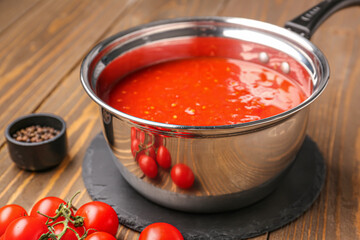 Saucepan with tasty tomato sauce on wooden background