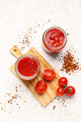 Jars with tasty tomato sauce on light background