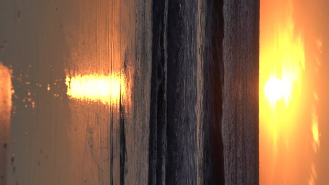 Vertical footage of ocean sunset on sandy beach and sunny path on water surface.