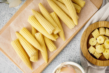 Wooden board with tasty canned corn cobs on light background