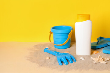 Fototapeta na wymiar Sunscreen cream for baby with beach accessories on sand near yellow wall