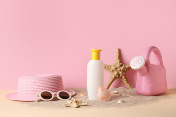 Sunscreen cream for baby with beach accessories on sand near pink wall