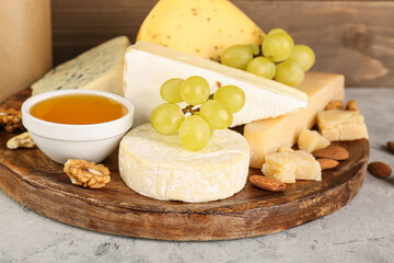 Plate with different types of cheese, honey and grapes on table