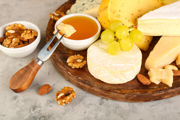 Plate with different types of cheese, honey and grapes on grunge background, closeup